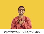 Small photo of Happy black man in glasses smiling and holding his hands on his chest to express endless gratitude and appreciation. Cheerful ethnic guy says thank you from the bottom of his heart for gift or present