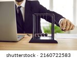 Small photo of Close up of business leader playing with Newton's cradle on office desk with notebook PC. Man moves black pendulum ball, it hits others, and kinetic energy is transferred into potential and vice versa