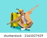 Happy man who goes on summer vacation by air poses with suitcase on light blue background. Guy in summer clothes sits with outstretched arms imitating flight of airplane. Air flight journey concept.