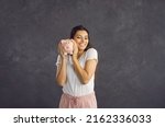 Smiling young Hispanic woman on black studio background hold piggybank with money investment. Happy millennial Latino female excited about saving in piggy bank. Financial stability concept.