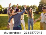 Small photo of Group of happy young people have fun together while walking in park on warm summer evening. Cheerful excited multiethnic friends laugh out loud and give each other high five.