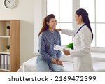 Friendly smiling female doctor touches patient's shoulder and tells her good news. Joyful young woman sitting on couch in doctor's office during medical examination and talking to doctor.