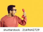 Small photo of Side view man with angry face expression shouting at stupid call center tech support service line helpdesk operator. Scared shocked terrified or enraged guy on yellow color holding old phone receiver