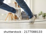 Small photo of Clumsy person falls down after stumbling over a power cable. Man or woman in sneakers trips over an electrical cord while walking on the floor at home. Cropped shot. Domestic accident concept