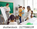 Small photo of Happy teacher and students having interesting class in classroom. Educator uses white board, gives short presentation, explains grammar rules and asks children some questions. Back to school concept