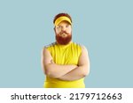 Small photo of Angry fat man in sportswear. Displeased sports coach standing with his arms crossed and looking at camera. Funny chubby guy with serious unsmiling face expression isolated on blue background
