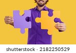 Small photo of Two big puzzle pieces in hands of man symbolize creation of cohesive team for company and events to build their own corporation, entrepreneur stand in yellow studio. Business concept
