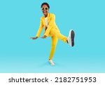 Small photo of Full body shot of happy funny cheerful positive attractive young African American woman wearing stylish yellow suit and cool sunglasses dancing isolated on blue background. Party and fashion concept