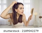 Small photo of Portrait of woman in her 20s or 30s looking at her reflection with scared nervous expression as she notices bad signs like scalp dandruff, hair thinning, or hair falling out. Hair loss problem