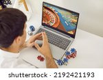 Young man playing poker on an online casino club website. Young guy sitting at a desk with poker chips and looking at the screen of his modern laptop computer. Online gambling and betting concept