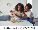 Small photo of Family plays board game. Cheerful and friendly young woman and her teenage daughter are having fun playing Jenga together. Dark-skinned family spending time together at home on day off.