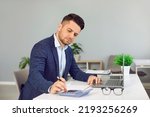 Small photo of Serious businessman in office calculates monthly expenses, taxes and sums up total amount. Man in fashionable suit works with laptop, calculator and paper documents at workplace. Own business