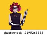 Small photo of Woman in Halloween costume with surprised expression showing copy space advert solution. Woman in peony wreath, Halloween makeup and gloves in form of hand brush advertises on orange background.