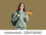Small photo of Overjoyed female student in hoodie with backpack and German flag enjoy study abroad. Smiling girl teenager isolated on green studio background pursue international education in Germany.