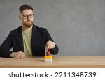 Serious man pushes big red button. Young hipster guy or businessman in glasses hits red alert button on table. Male entrepreneur sitting at desk presses activation button to get access to something