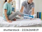 Small photo of Woman with a splint on her shin lies on a couch in the physiotherapist's office in the rehabilitation center. Male physiotherapist examines a patient's leg during a rehabilitation consultation