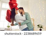 Happy, cheerful couple in love celebrating St Valentine's Day. Joyful, positive young man and woman enjoying Saint Valentine's Day, hugging, dancing with red heart shaped balloons, having fun together
