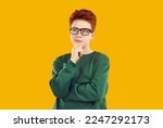 Small photo of Thoughtful teenage boy standing with his hand on chin. Handsome puzzled redhead boy wearing glasses posing with serious face expression over yellow isolated background
