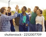 Friendly gesture. Group of happy young people give each other high five during meeting on city street. Cheerful African American woman greets her Caucasian male friend surrounded by their best friends