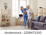 Small photo of Life of pensioner in modern specialized nursing home. Friendly young female caregiver who cares for elderly man in nursing home helps him get up from sofa. Elderly care concept. Side view.