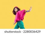 Small photo of Happy child dancing. Cheerful little African American girl wearing loose oversized fuschia top and green jeans with trendy eyelet belt dancing isolated on solid yellow background. Kids fashion concept