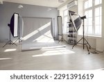Photo session studio. Photographer's workplace in commercial atelier agency. Sunny workspace interior with grey backdrop, backstage and lamp, umbrella, flashlight illumination equipment kit. No people