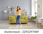 Overjoyed girl wearing headphones listening to music and dancing. Happy positive girl in casual clothes having fun and relaxing in living room at home. Woman enjoying music and leisure weekend