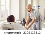 Small photo of Friendly hospital staff gives intravenous vitamin course infusion to patient. Smiling nurse personnel puts IV line venous needle in vein of relaxed adult male lying and resting on bed in medical ward