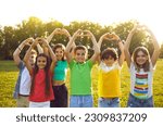 Small photo of Happy children wish for world peace. Cheerful healthy kids standing on camp field or park lawn in sunset or sunrise sunlight look at camera, smile, raise hands up and do heart gestures. Group portrait