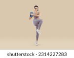 Small photo of Athletic positive Caucasian woman training with dumbbells gives exercise to stretch muscles by raising knees up wearing tight fitness clothes stands in beige studio. Healthy and sports lifestyle