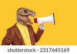 Small photo of Side view man in funny crazy carnival masquerade tyrannosaurus dinosaur reptile face mask on yellow studio background speaks through megaphone with loud voice, shares message, calls to holiday event