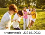 Happy children play games in park on sunny summer day. Cheerful kids meet on green field or meadow, hold rope, play tug of war, compete with each other, enjoy challenge, make effort. Teamwork concept