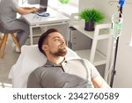 Small photo of Male patient receives intravenous medical infusion at clinic or hospital. Young man lying on bed and getting medication or vitamin solution through sterile IV line. Medicine, therapy treatment concept