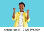 Small photo of Happy excited emotional african american woman sincerely happy isolated on light blue background. Young ethnic woman in casual clothes squeals with happiness and clenches her fists joyfully