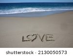 Small photo of Words written in beach sand. The word LOVE written in the sand on the beach with the ocean as the background. Love is all you need. Everyone Loves the beach. Love.