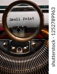 Small photo of Vintage typewriter with the words small print printed on a letter and a mans hand holding a magnifying glass