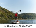 A girl in a bright life jacket on a SUP board with an oar in her hands enjoys her vacation. High quality photo