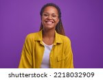 Young cute happy African American woman zoomer in casual clothes laughing and looking at camera radiating optimism and positive emotions stands on plain purple background. Good mood concept