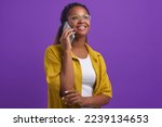 Young positive ethnic African American woman in glasses with smile looks up making phone call and flirting with boyfriend or work colleague dressed in casual style stands posing in lilac studio