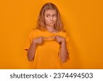 Small photo of Young shy cute Caucasian woman teenager looks awkwardly to side feeling awkward and puts fingers together in front of chest dressed in casual yellow shirt stands on plain yellow background.