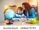 Family at home. Children doing homework with books, textbooks, mother help to kids. Mother helping her son making school homework at home. Home schooling and concept of COVID-19 pandemic infection
