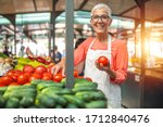 Woman tending an organic vegetable stall at a farmer's market and selling fresh vegetables. Female gardener selling organic crops and picking up a bountiful basket full of fresh produce. Only organic.