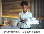 Maid putting stack of fresh white bath towels on the bed sheet. Room service maid cleaning hotel room. Maid making bed in hotel room. Change of towels in the hotel room
