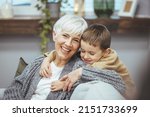 Small photo of Grandma and grandson spend time together watching a funny video or cartoon on the phone, laughing while grandson hugs her. They enjoy their modern home.