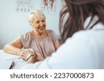 Small photo of Doctor giving hope. Close up shot of young female physician leaning forward to smiling elderly lady patient holding her hand in palms. Woman caretaker in white coat supporting encouraging old person