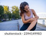 Small photo of Woman with knee pain in a park. Female athlete suffering form running knee or kneecap injury during outdoor workout. Woman sitting on ground and holding knee