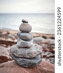 Small photo of Cairn Pile of stacked red and brown coloured granite stones or pebbles on the beach with grey sea and sky in the background