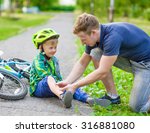 Small photo of father putting band-aid on young boy's injury who fell off his bicycle.