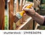 Small photo of Painting protective varnish on wooden picket fence at backyard. Man paint wood stain at timber plank outdoors