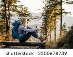 Woman with backpack and thermos resting on bench in forest. Relaxation during hiking in mountain